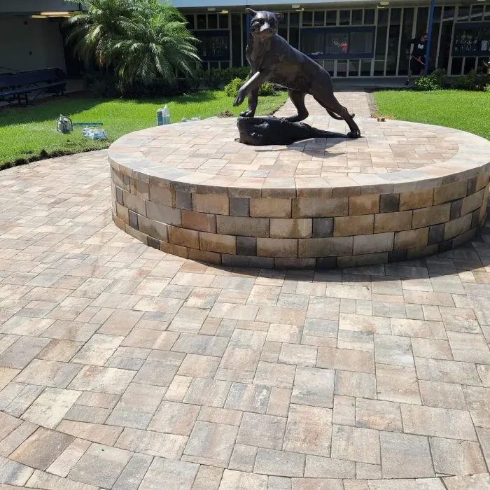 Circular paver plaza around a raised stone planter with a statue
