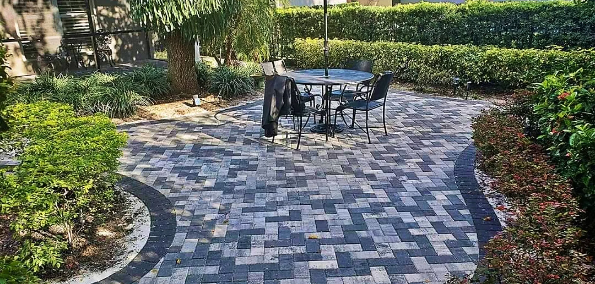 Circular herringbone paver patio with a bistro table, framed by hedges
